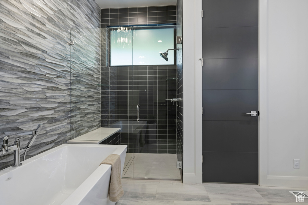 Bathroom featuring shower with separate bathtub, tile flooring, and tile walls