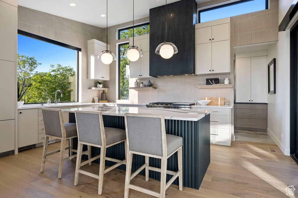 Kitchen with backsplash, hanging light fixtures, light hardwood / wood-style flooring, and a kitchen island