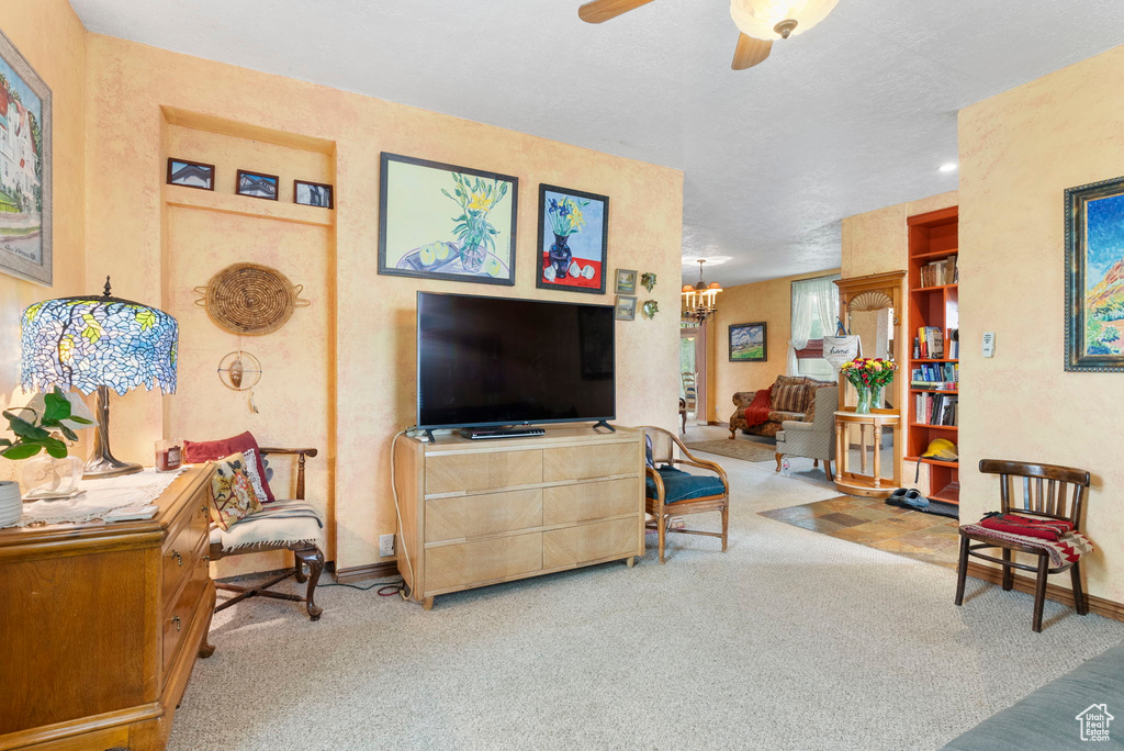 Carpeted living room featuring a textured ceiling and ceiling fan with notable chandelier