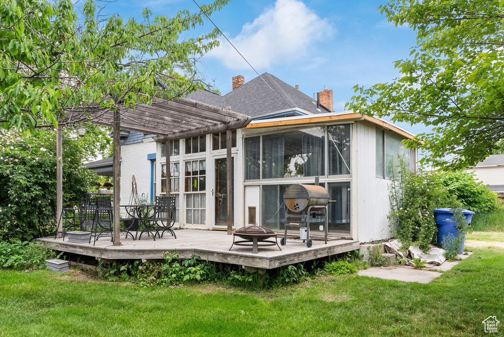 Rear view of house with a sunroom, a pergola, a deck, and a lawn