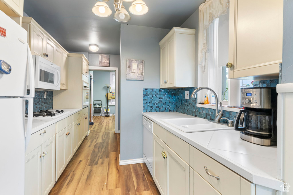 Kitchen featuring light hardwood / wood-style floors, backsplash, a notable chandelier, sink, and white appliances