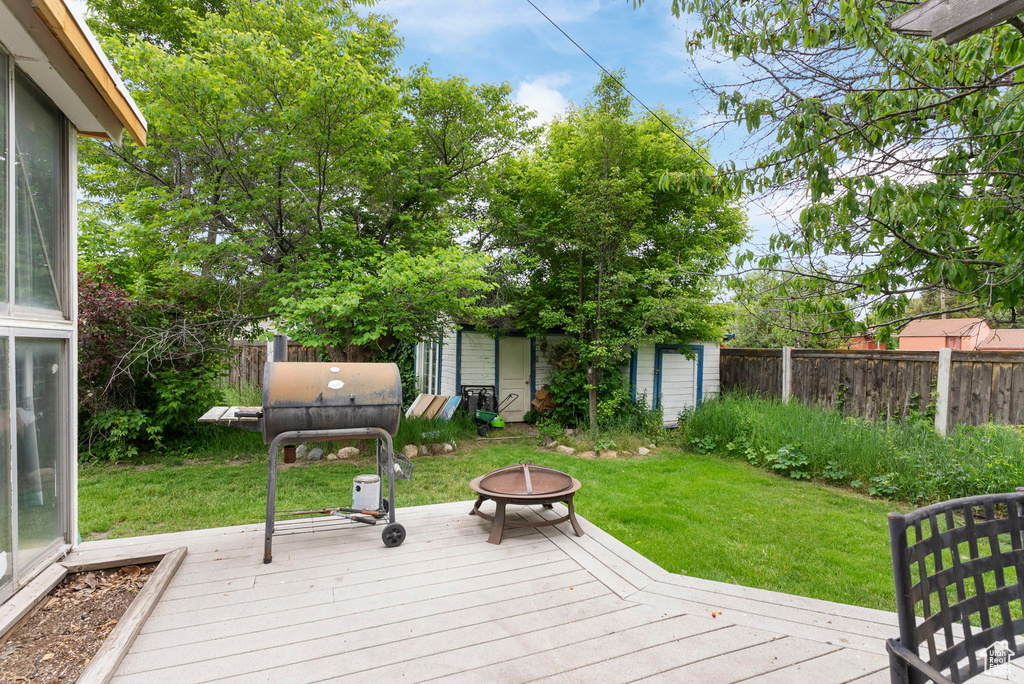 Wooden terrace featuring a grill, an outdoor structure, and a fire pit