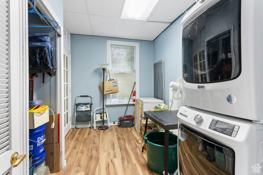 Laundry area with light hardwood / wood-style flooring and stacked washer / drying machine