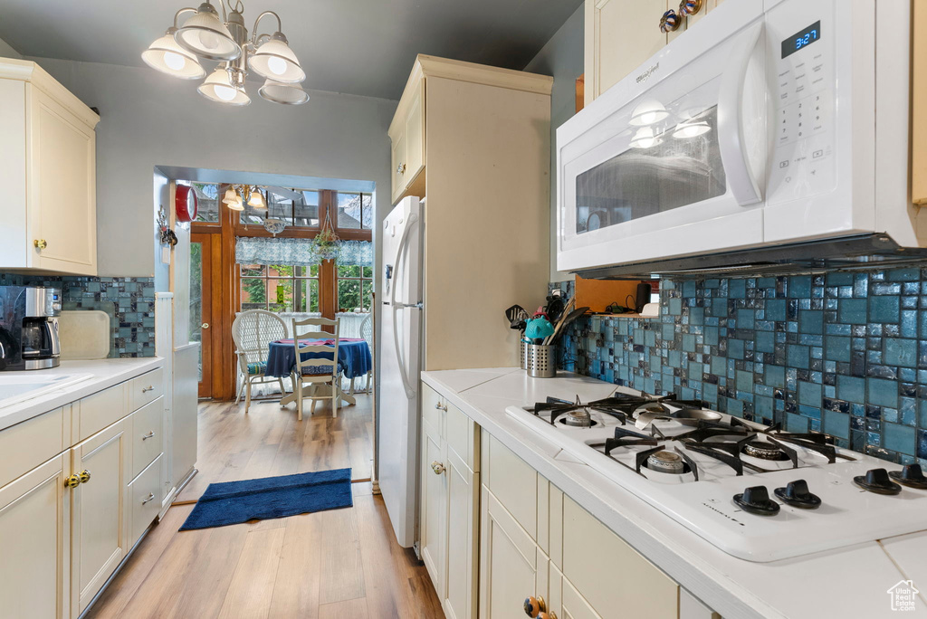 Kitchen with light wood-type flooring, white appliances, cream cabinets, backsplash, and a chandelier