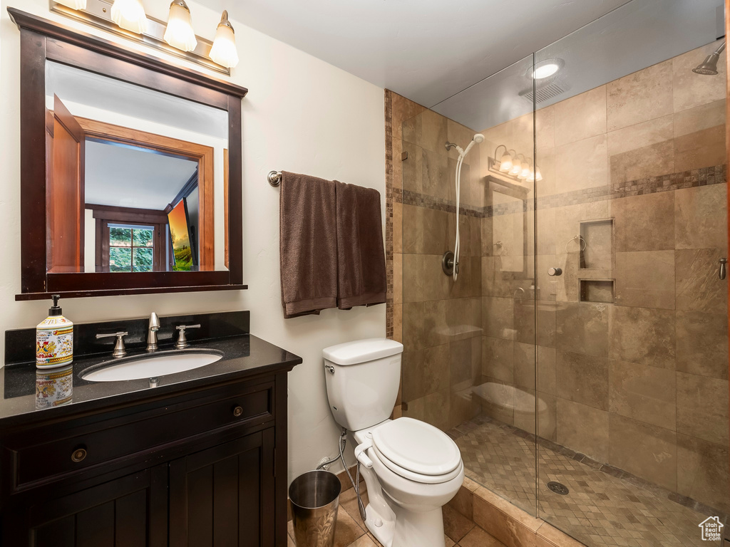 Bathroom featuring a shower with shower door, vanity, toilet, and tile floors