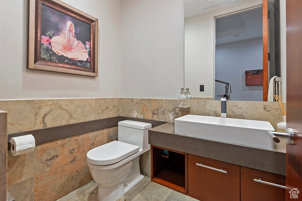 Bathroom with tile walls, tile flooring, vanity, and toilet