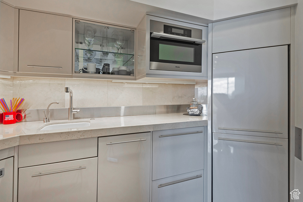 Kitchen with light stone countertops, sink, backsplash, and paneled built in refrigerator