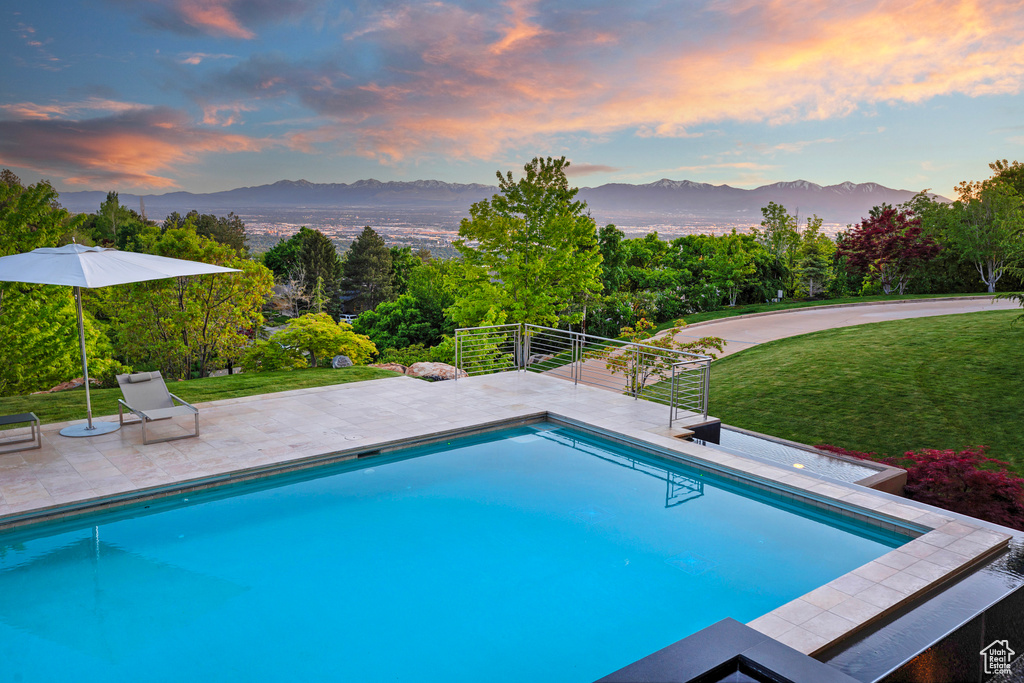 Pool at dusk featuring a mountain view and a lawn