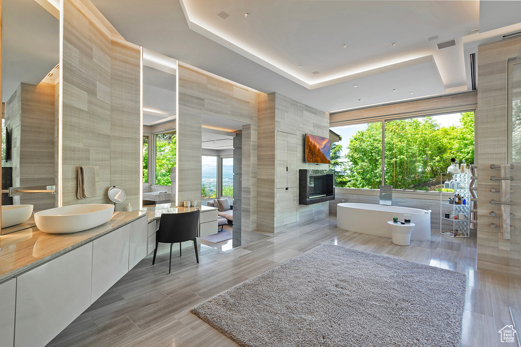 Bathroom with separate shower and tub, tile walls, a raised ceiling, a multi sided fireplace, and vanity