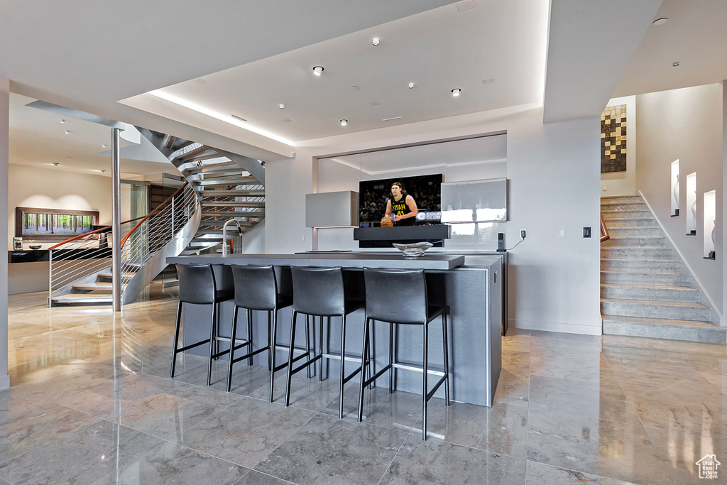 Kitchen with an island with sink, a raised ceiling, a breakfast bar area, and light tile floors