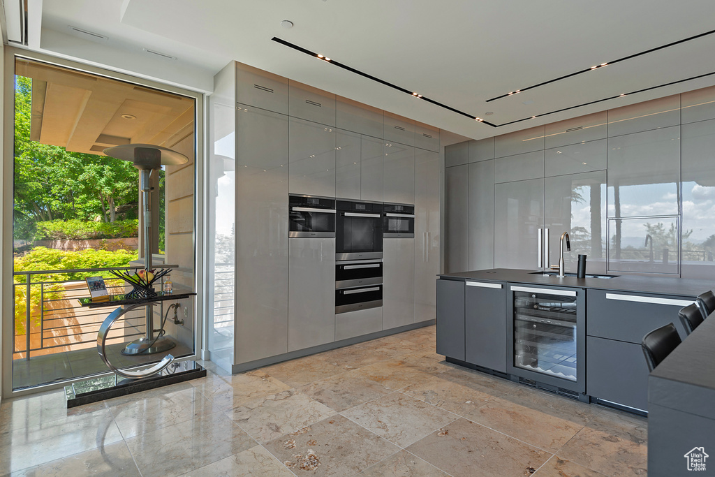 Kitchen featuring gray cabinetry, beverage cooler, sink, multiple ovens, and light tile floors