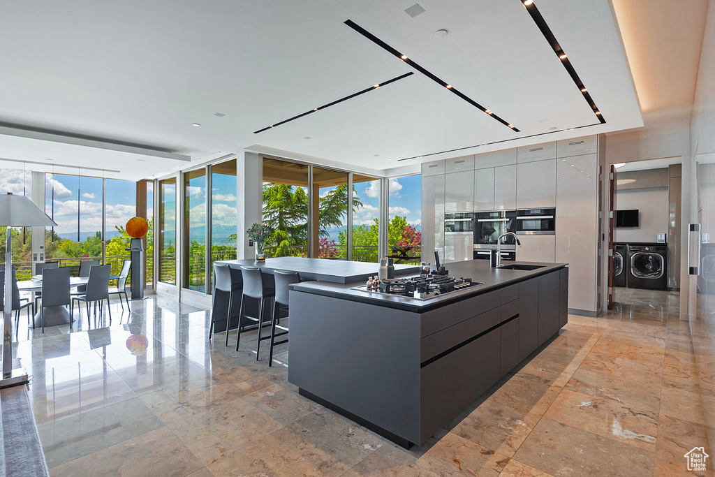 Kitchen with floor to ceiling windows, light tile flooring, stainless steel gas cooktop, and a kitchen island with sink