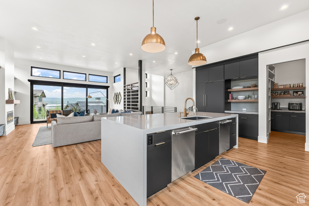 Kitchen featuring stainless steel dishwasher, light hardwood / wood-style flooring, a kitchen island with sink, pendant lighting, and sink