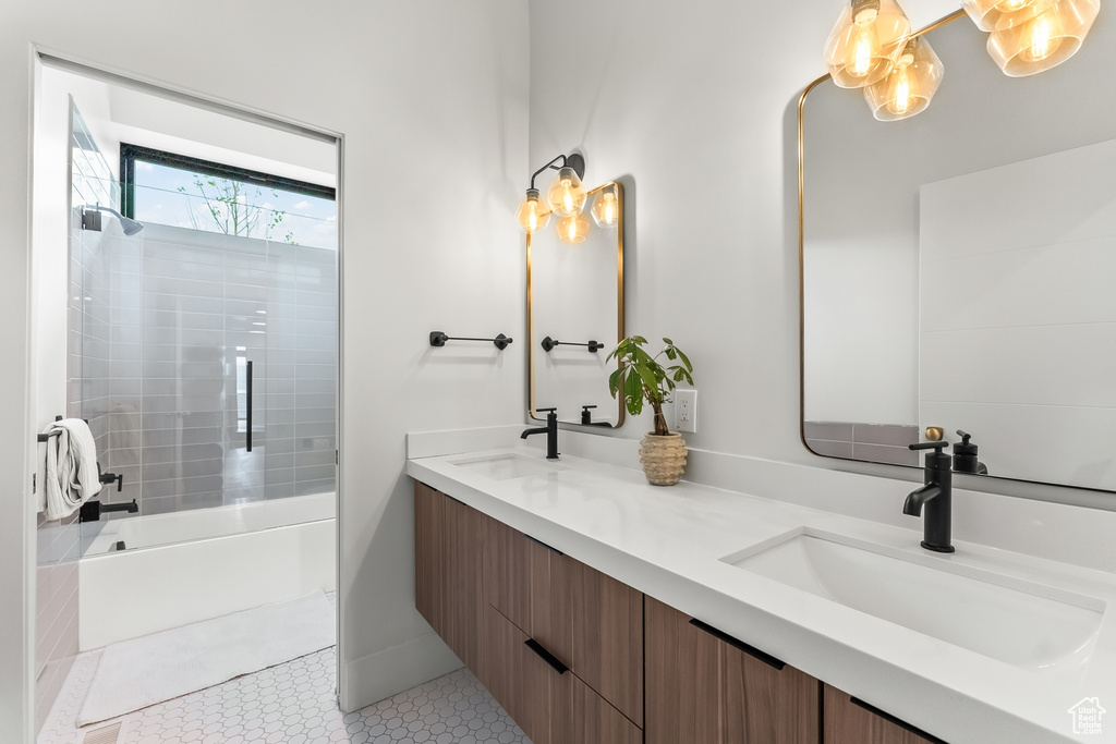 Bathroom featuring vanity with extensive cabinet space, dual sinks, tiled shower / bath combo, and tile floors