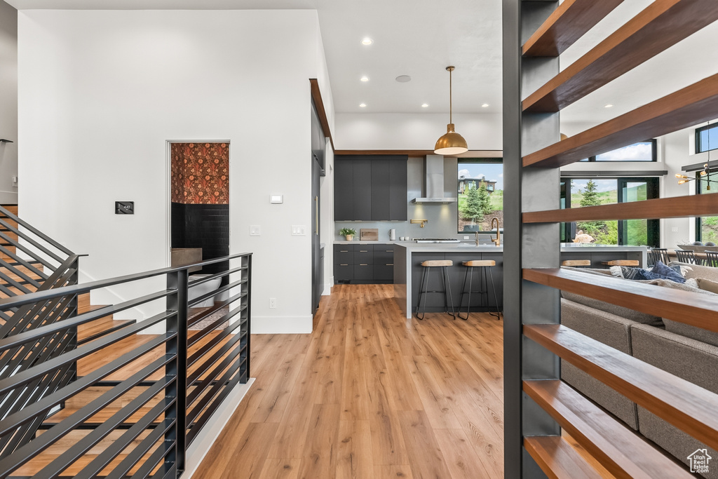 Kitchen with a towering ceiling, wall chimney range hood, hanging light fixtures, light wood-type flooring, and sink