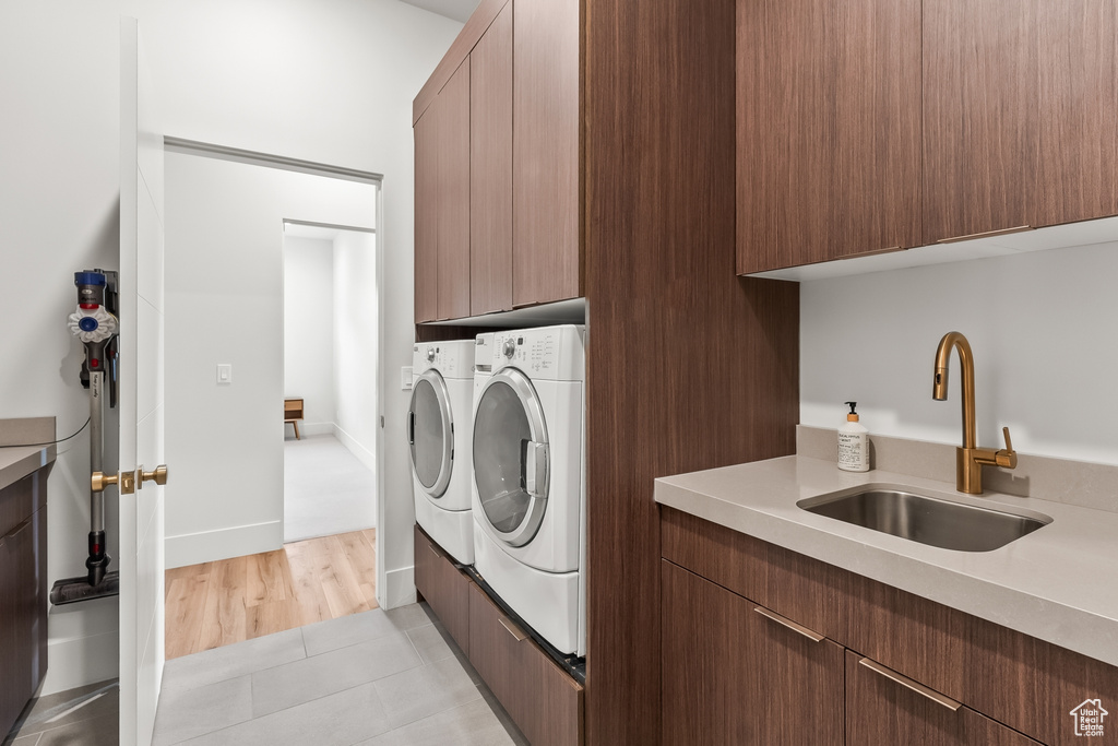 Laundry area with sink, light hardwood / wood-style flooring, washing machine and clothes dryer, and cabinets