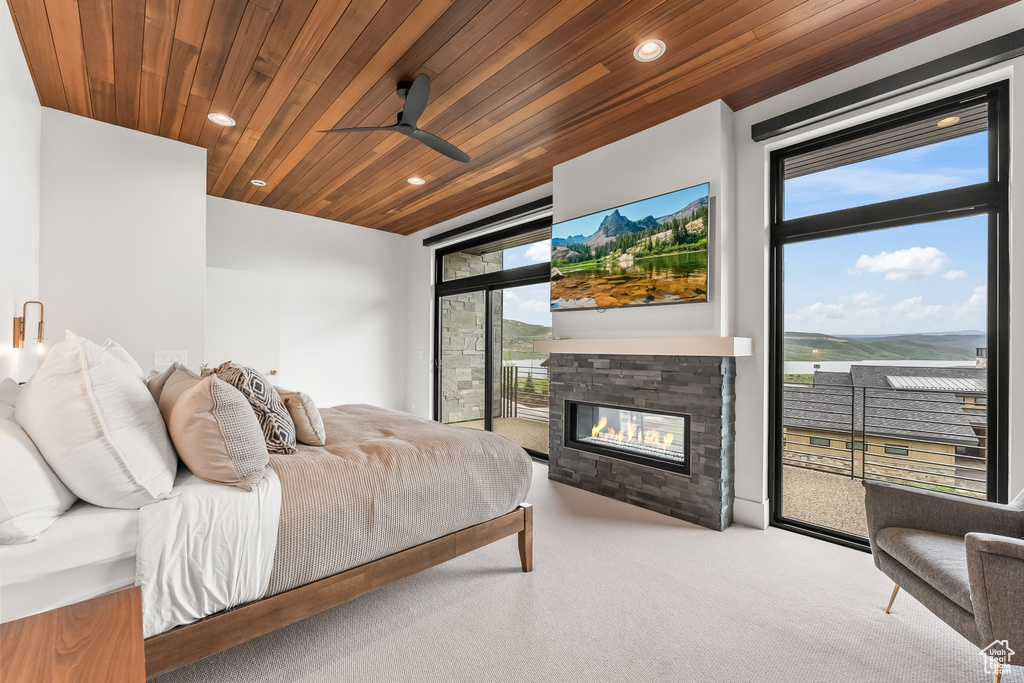 Bedroom featuring ceiling fan, carpet floors, expansive windows, a fireplace, and wood ceiling