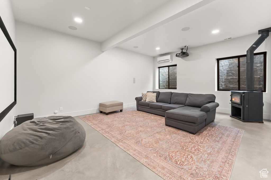 Living room featuring beam ceiling, concrete flooring, a wood stove, and a wall mounted air conditioner