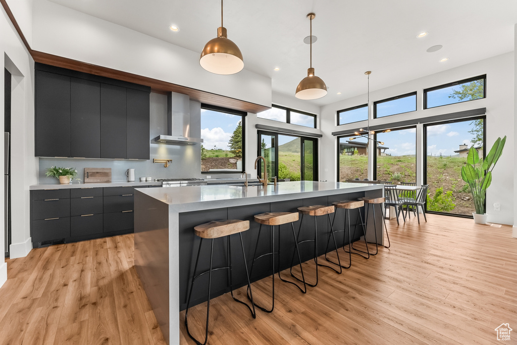 Kitchen with a wealth of natural light, wall chimney range hood, light wood-type flooring, and pendant lighting