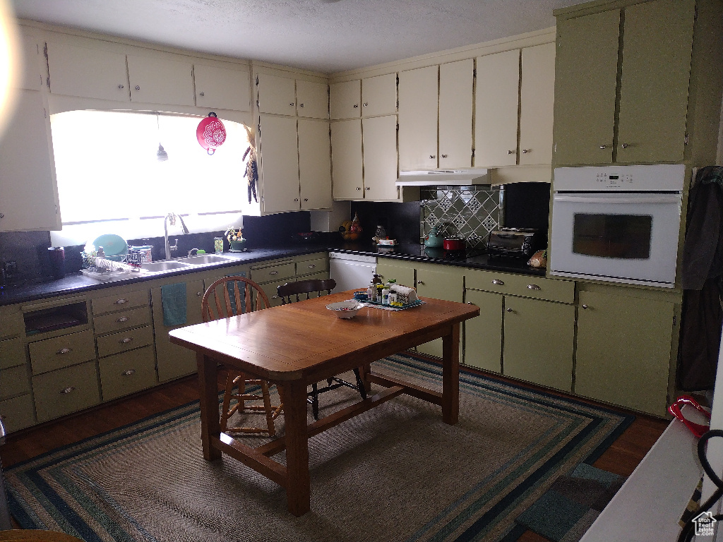 Kitchen with dark hardwood / wood-style floors, dishwashing machine, backsplash, oven, and sink