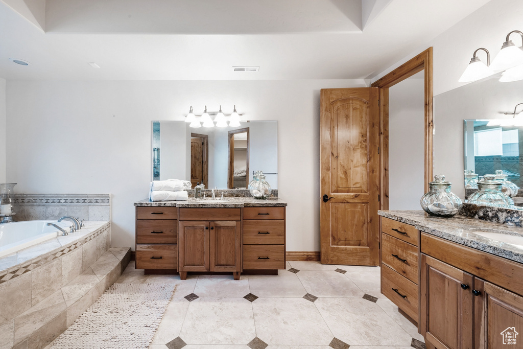 Bathroom featuring double vanity, tiled tub, and tile flooring