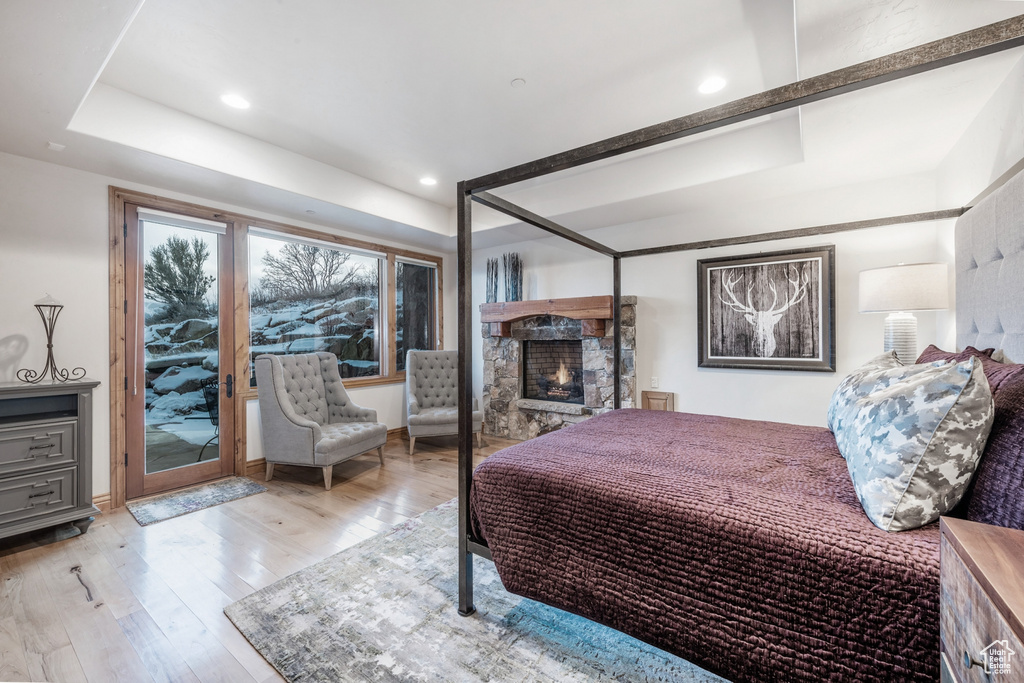 Bedroom with access to outside, a stone fireplace, and light wood-type flooring