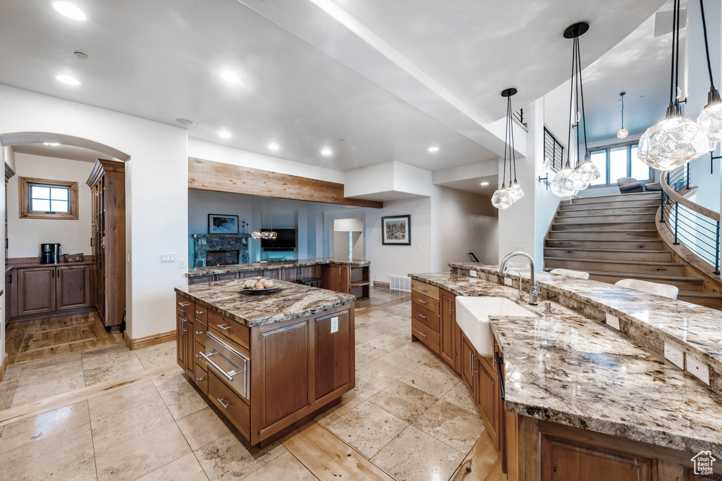 Kitchen with a fireplace, a large island, pendant lighting, sink, and light tile flooring