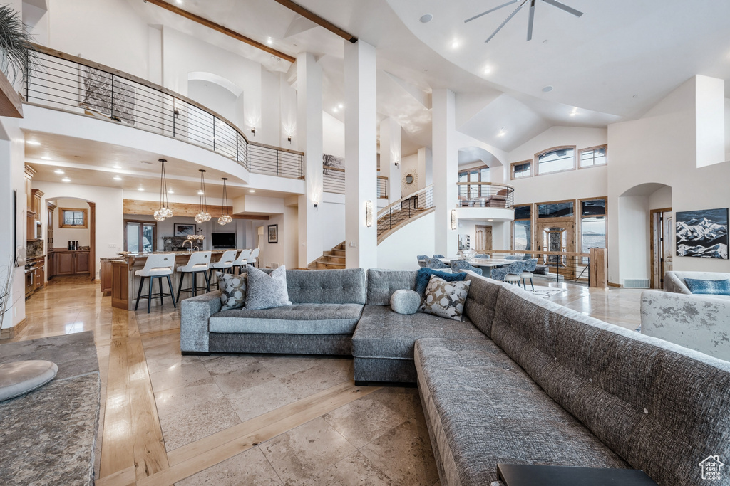 Living room featuring a high ceiling, light tile floors, and ceiling fan with notable chandelier