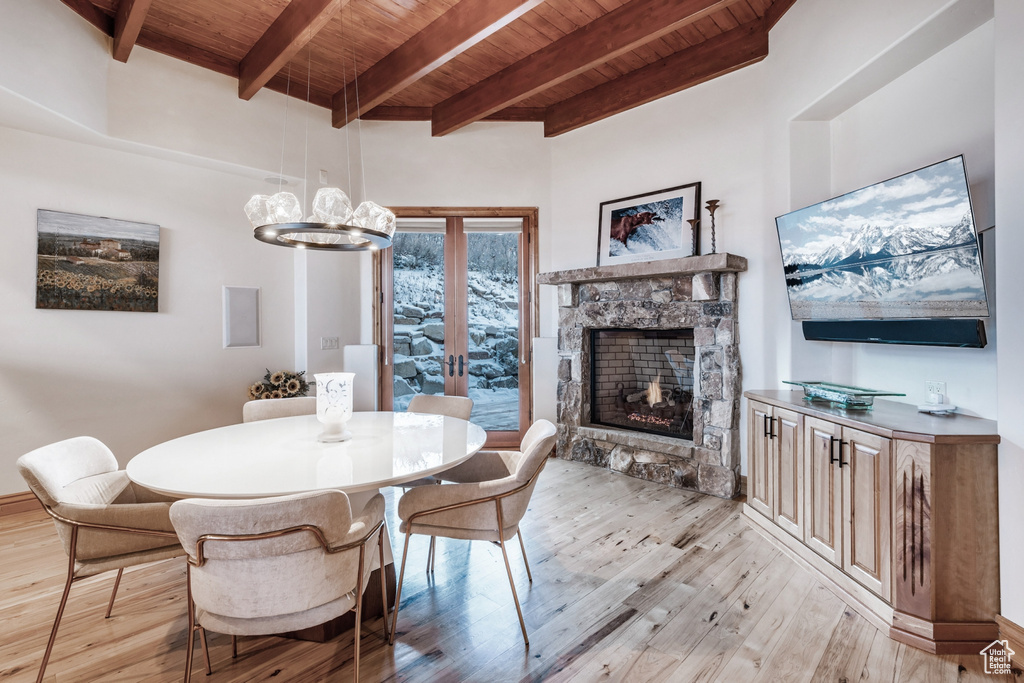 Dining space featuring a stone fireplace, wooden ceiling, beam ceiling, and light hardwood / wood-style flooring