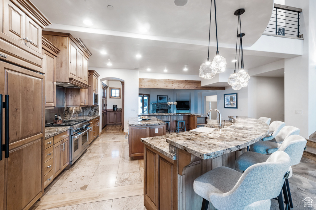 Kitchen with a kitchen island with sink, decorative light fixtures, high end appliances, stone counters, and light tile floors