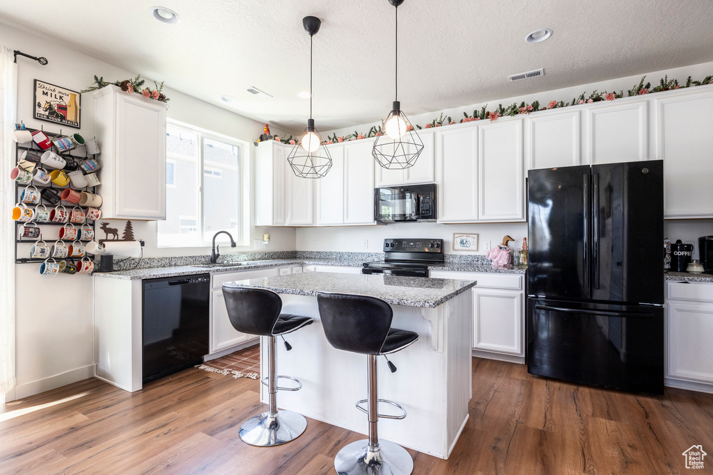 Kitchen with a center island, white cabinetry, hardwood / wood-style floors, and black appliances