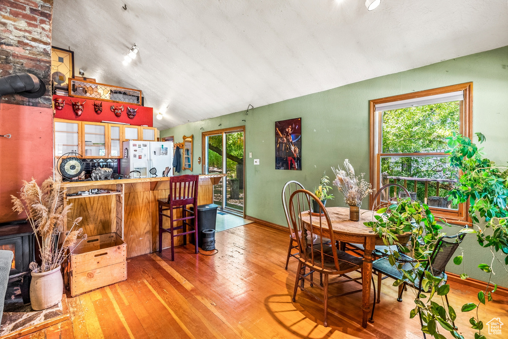 Dining space with brick wall, a wealth of natural light, hardwood / wood-style flooring, and lofted ceiling