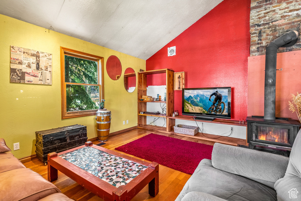 Living room featuring high vaulted ceiling, hardwood / wood-style floors, a wood stove, and brick wall