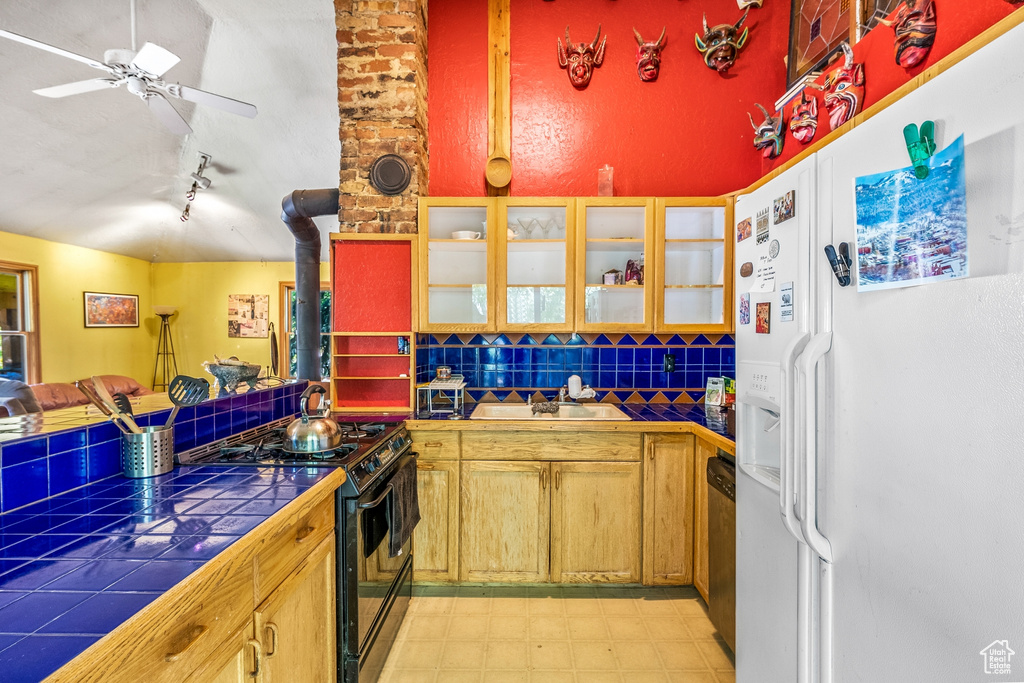 Kitchen featuring white refrigerator with ice dispenser, tasteful backsplash, tile counters, range with two ovens, and brick wall