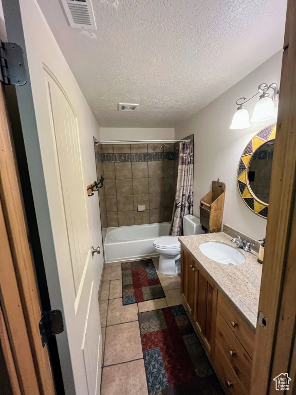 Full bathroom featuring tile flooring, a textured ceiling, shower / tub combo with curtain, toilet, and vanity