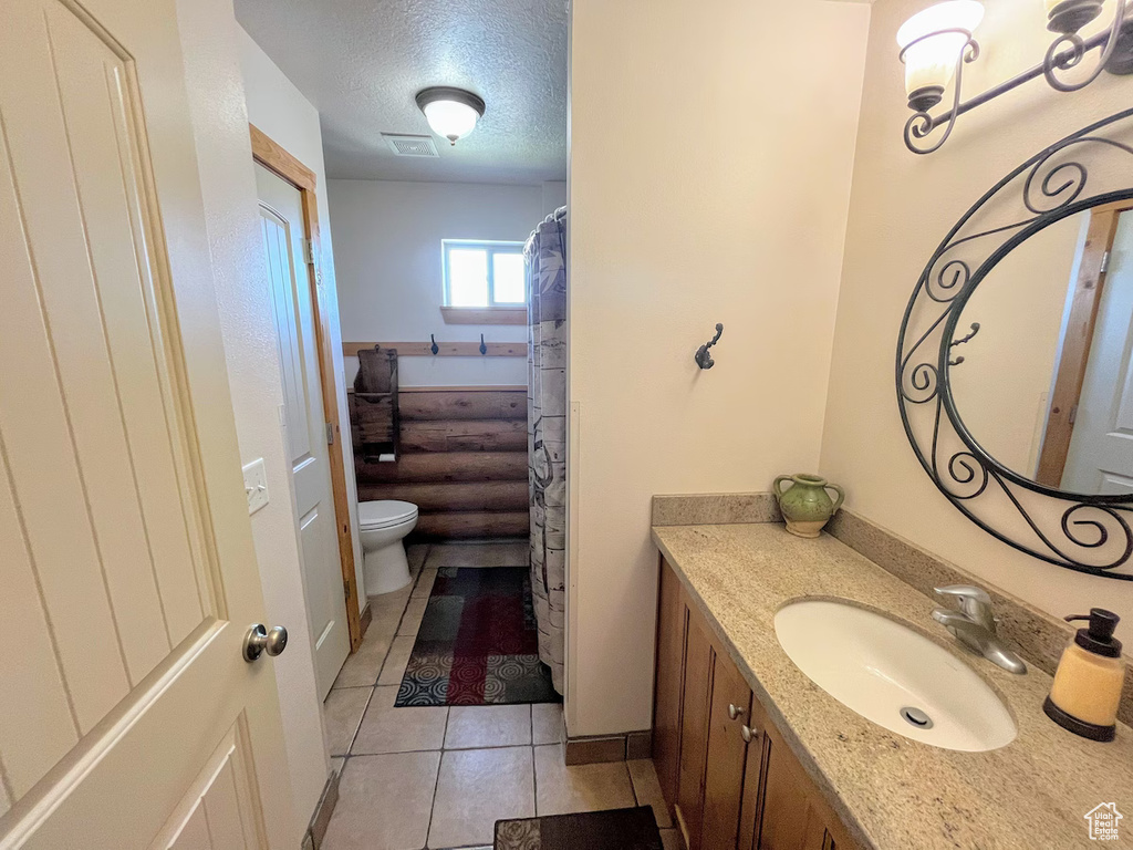 Bathroom with tile flooring, vanity with extensive cabinet space, a textured ceiling, and toilet