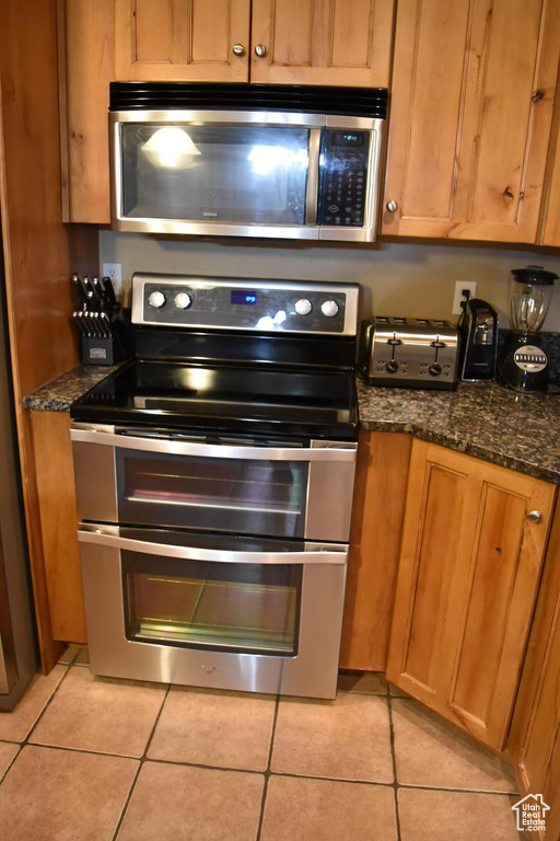 Kitchen featuring appliances with stainless steel finishes, dark stone counters, and light tile flooring