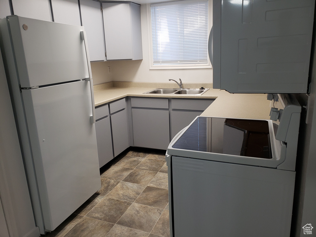 Kitchen with white fridge, tile floors, range, white cabinetry, and sink