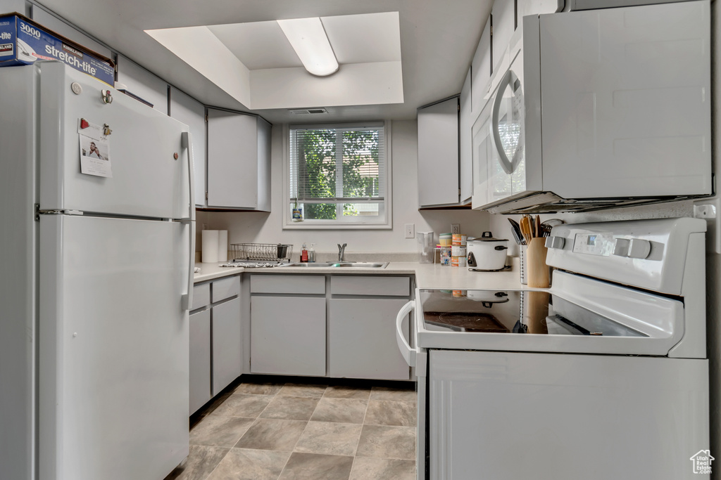 Kitchen with sink, white appliances, and light tile floors