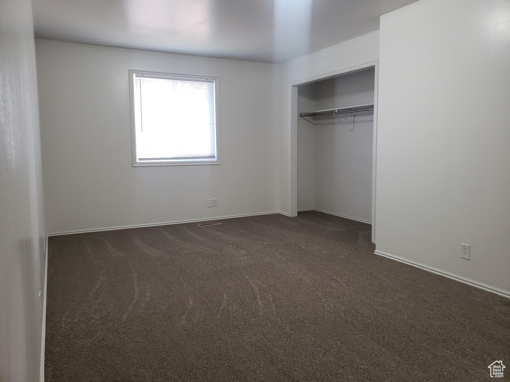 Unfurnished bedroom with dark carpet and a closet