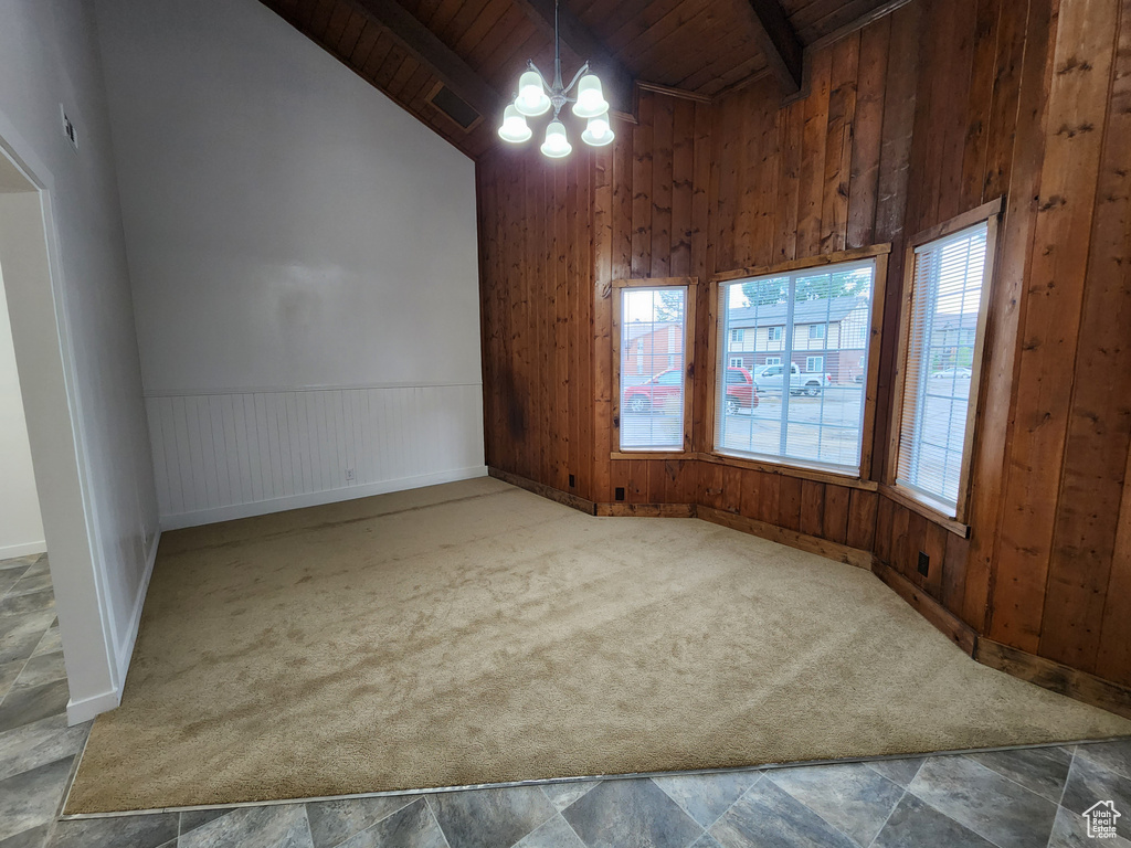 Empty room with beamed ceiling, wood walls, a notable chandelier, carpet flooring, and wood ceiling