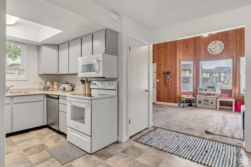 Kitchen featuring a skylight, sink, white appliances, and light tile floors