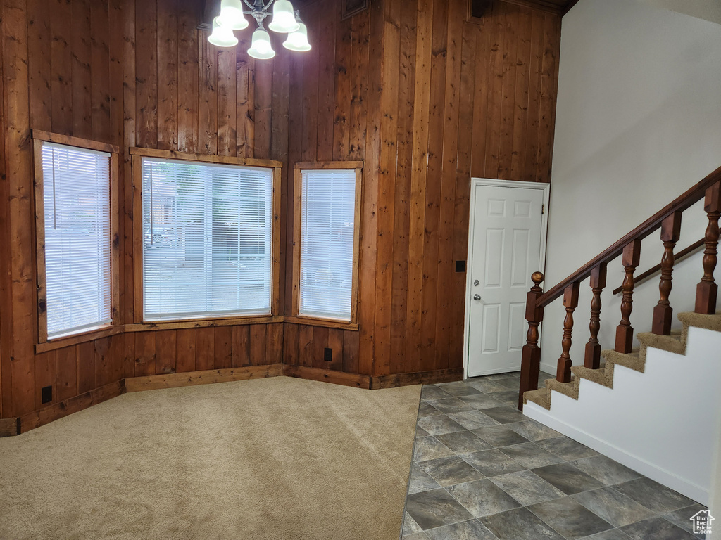 Entrance foyer featuring high vaulted ceiling, dark tile flooring, a notable chandelier, and wood walls