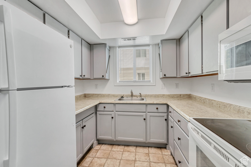 Kitchen with gray cabinetry, sink, white appliances, and light tile floors