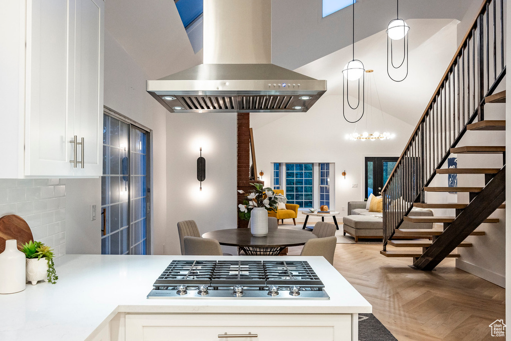 Kitchen featuring parquet floors, decorative light fixtures, stainless steel gas stovetop, island range hood, and a towering ceiling