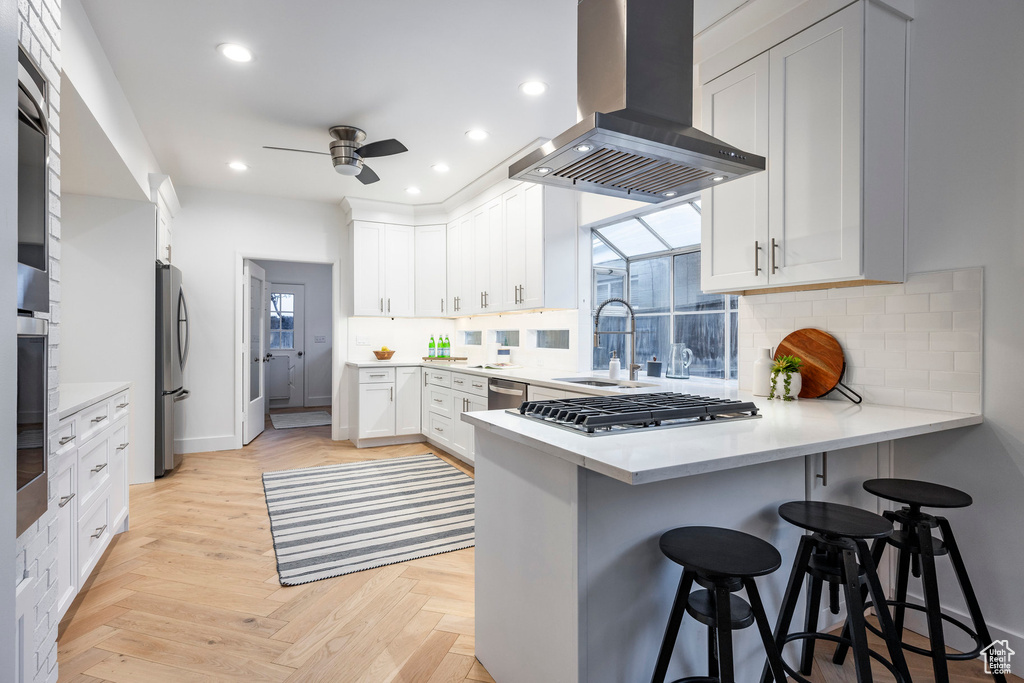 Kitchen featuring stainless steel appliances, light parquet flooring, a kitchen bar, range hood, and backsplash