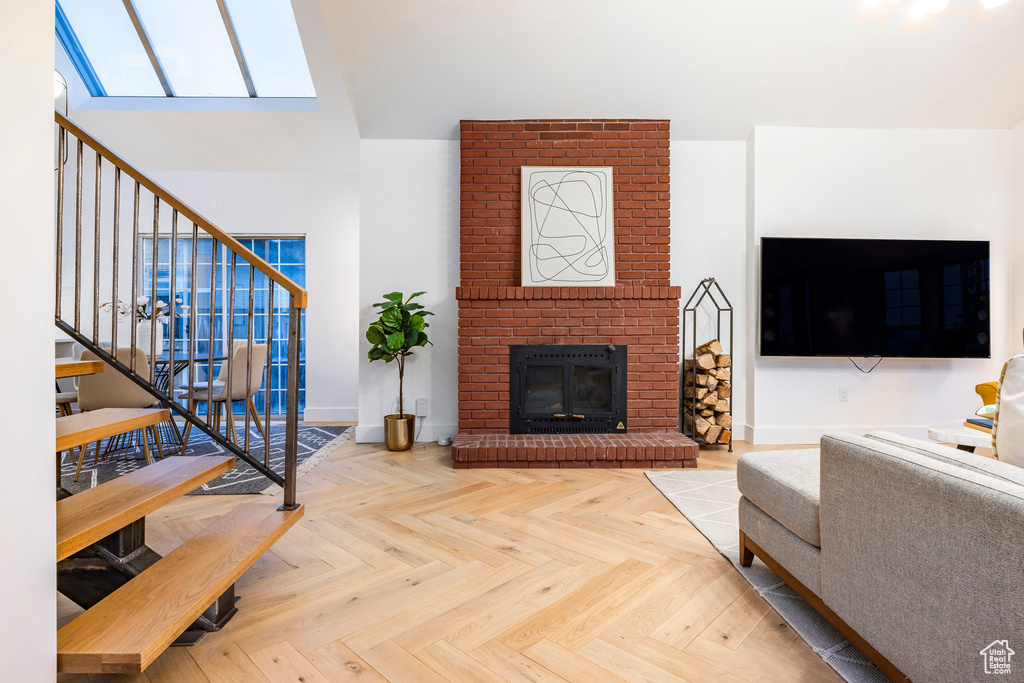 Living room featuring brick wall, a fireplace, light parquet flooring, and a skylight