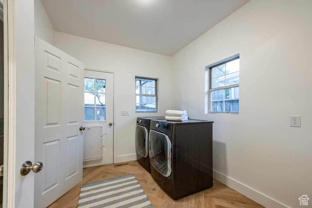 Clothes washing area featuring washing machine and clothes dryer and light parquet flooring