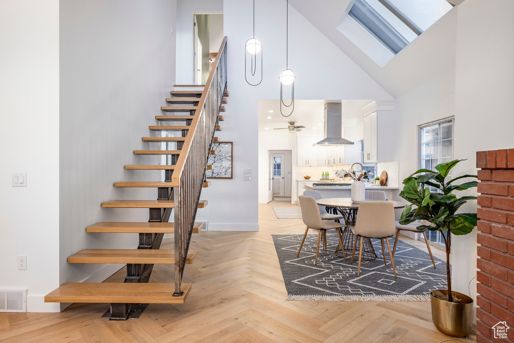 Dining space featuring light parquet floors, ceiling fan, a skylight, and high vaulted ceiling