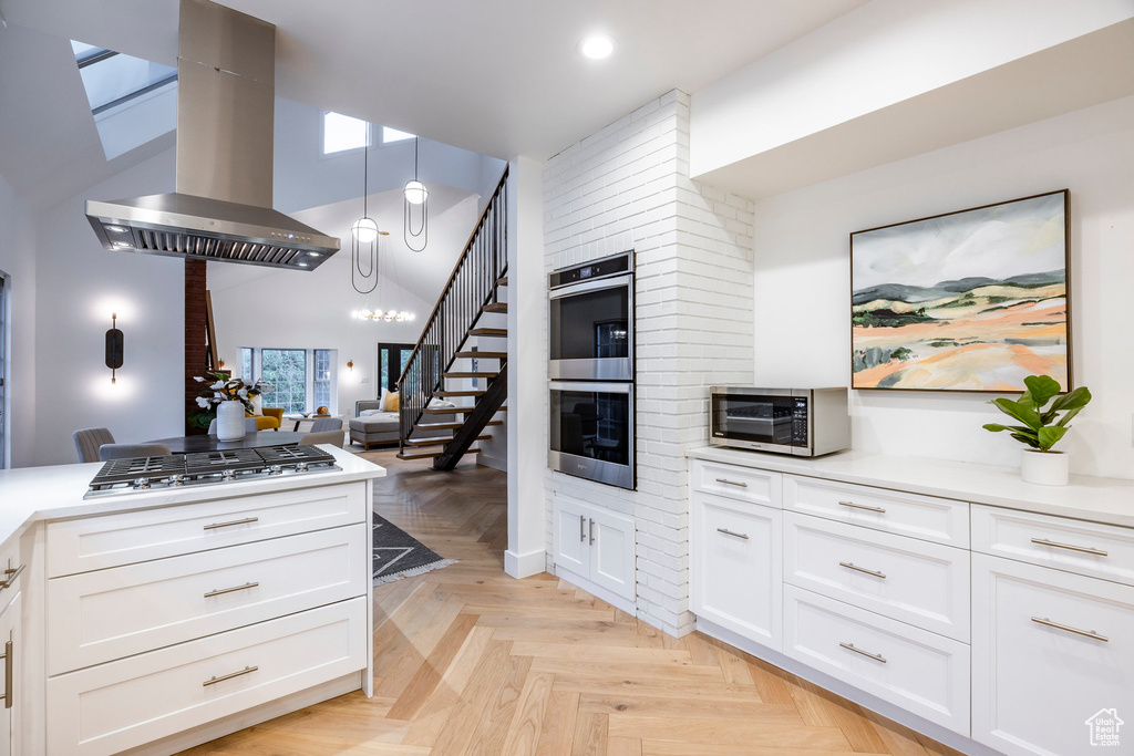 Kitchen featuring white cabinetry, decorative light fixtures, light parquet flooring, appliances with stainless steel finishes, and island range hood